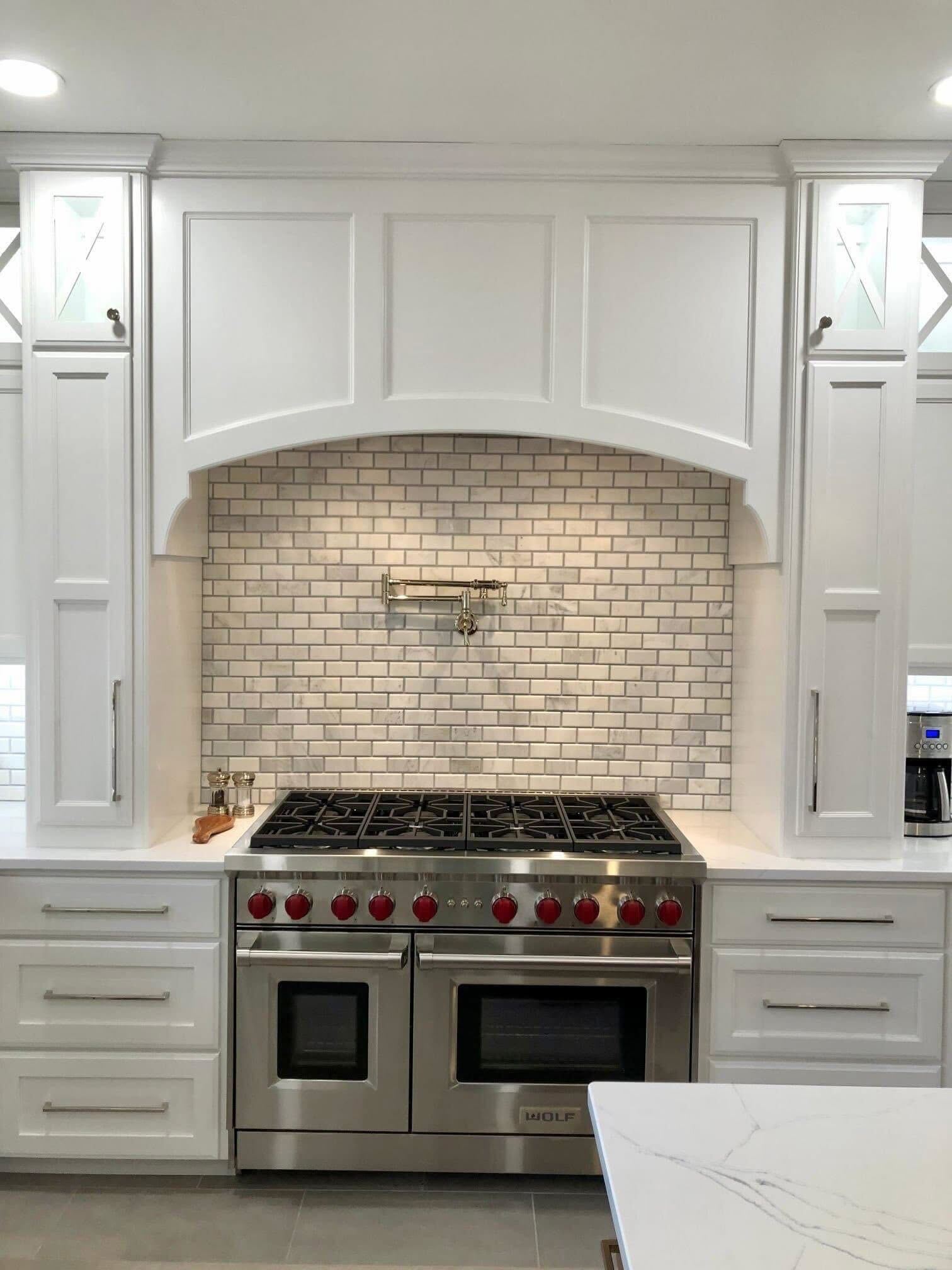 Custom white range hood surround with Wolf stove and subway tile backsplash